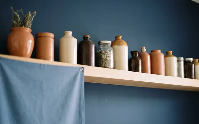 Ceramic and glass jars lined along a pale wooden shelf against a navy wall