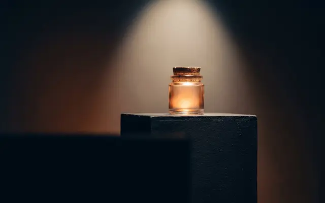 A single glass jar glowing amber on a dark pedestal under a narrow spotlight