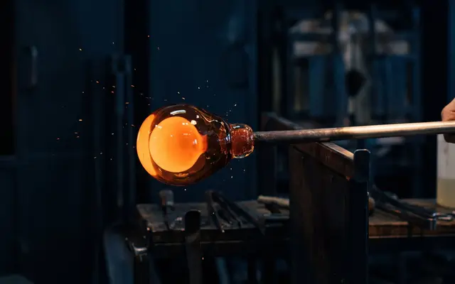 A glowing orange gather of molten glass on the end of a blowpipe in a dark studio