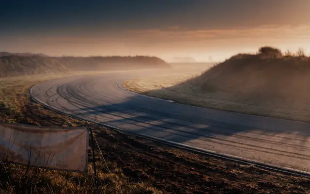 A sweeping curve of race track through misty hills at sunrise