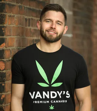 Steve VanDeWalle, founder of Vandy's, in a black Vandy's Premium Cannabis T-shirt against a brick wall